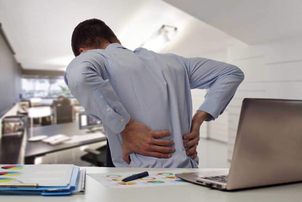 man in office holding back to demonstrate back pain