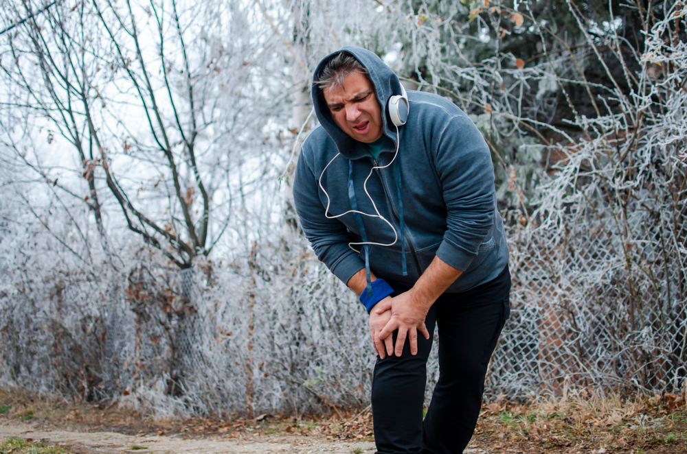 man with pain in the knee while running outdoors in cold day