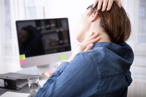 female teacher at desk stretching her neck with neck pain