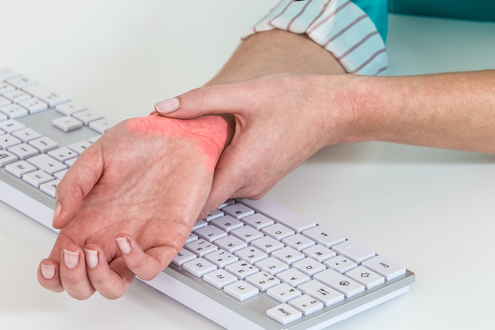 Woman at desk holding wrist in pain from carpal tunnel syndrome